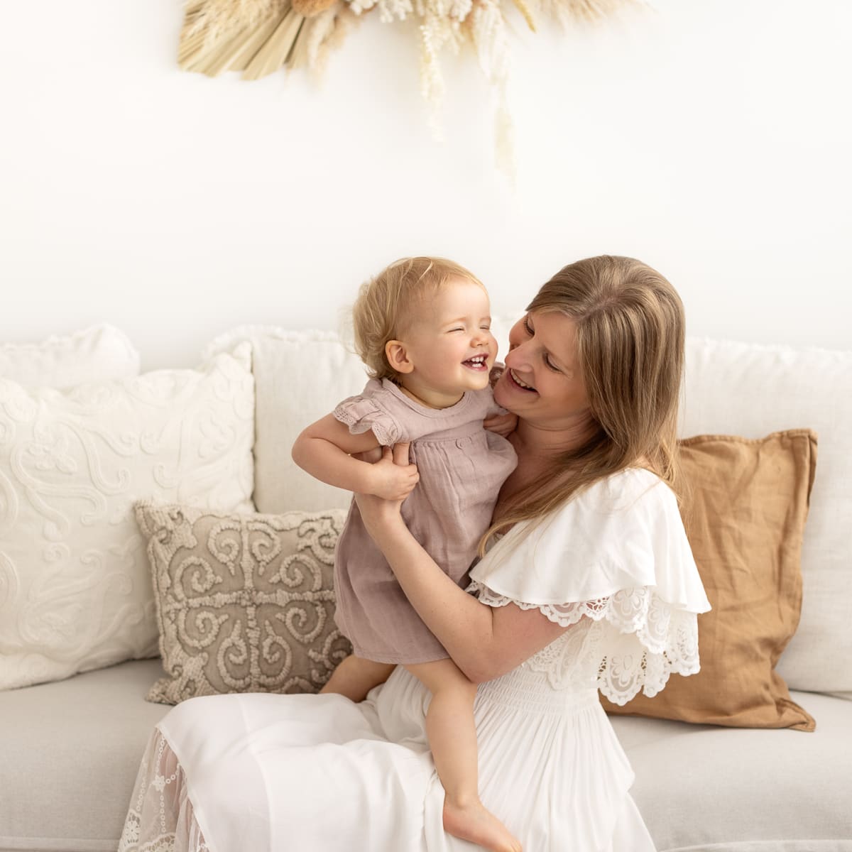 Mum and little girl laugh and cuddle on linen couch in boho styled melbourne photography studio