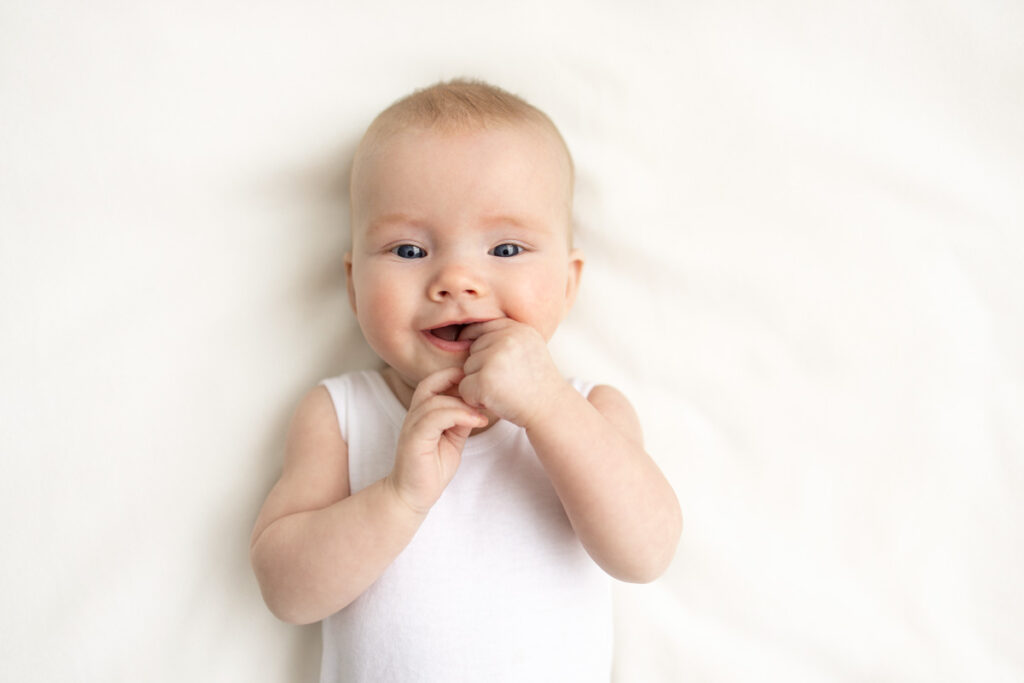 baby in white singletsuit smiling with hands in mouth in Melbourne photography studio