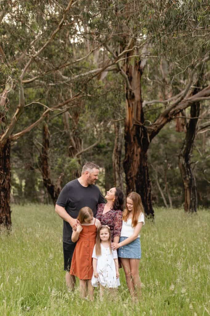 Family of five all hugging as Mum and Dad look at each other during outdoor sunset family photography session in Pakenham Victoria