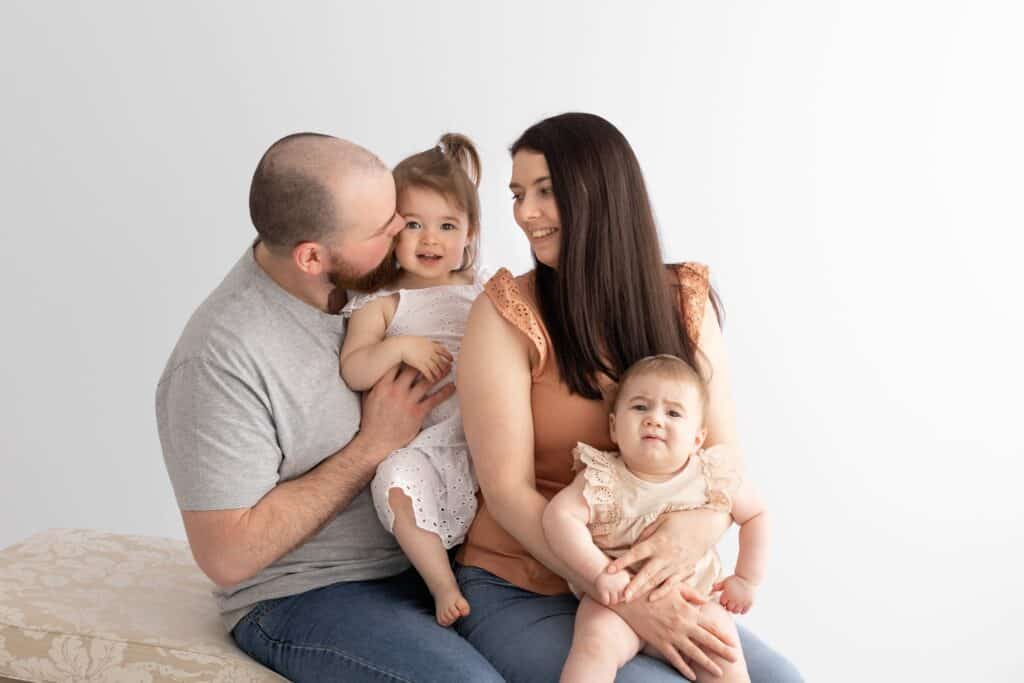 Family of four with two young girls cuddle during family photography session in white studio in Pakenham Victoria