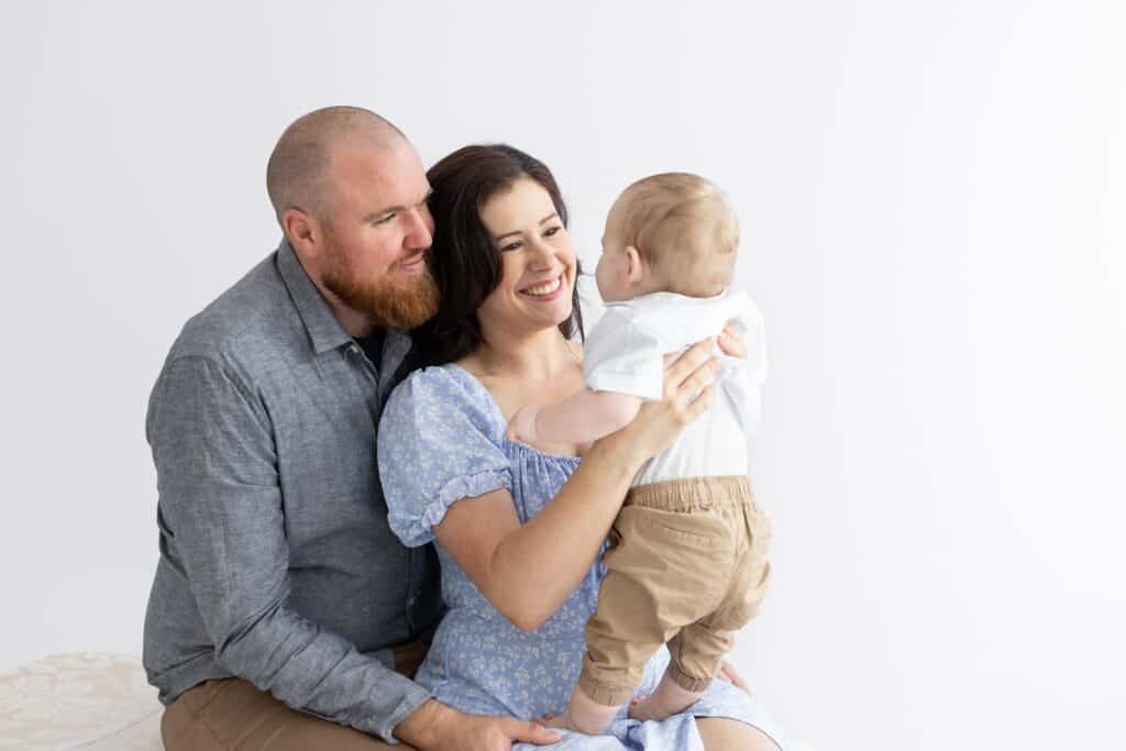 Parent looking lovingly at their 10 month old boy during family photography session in white studio in Pakenham Victoria