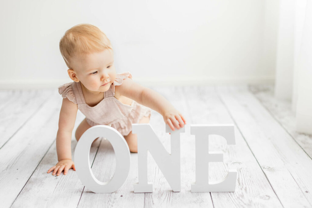 Baby girl reaching for white wooden ONE letters in white melbourne photography studio for 1st birthday session