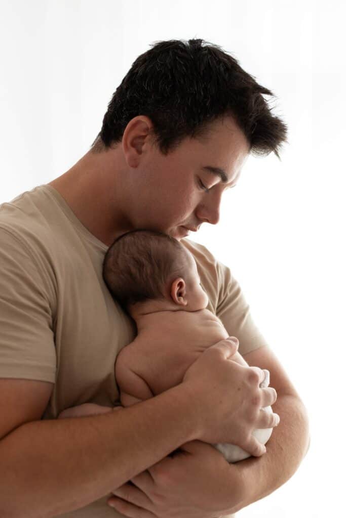 Father holding embracing new baby in white newborn photography studio in Melbourne