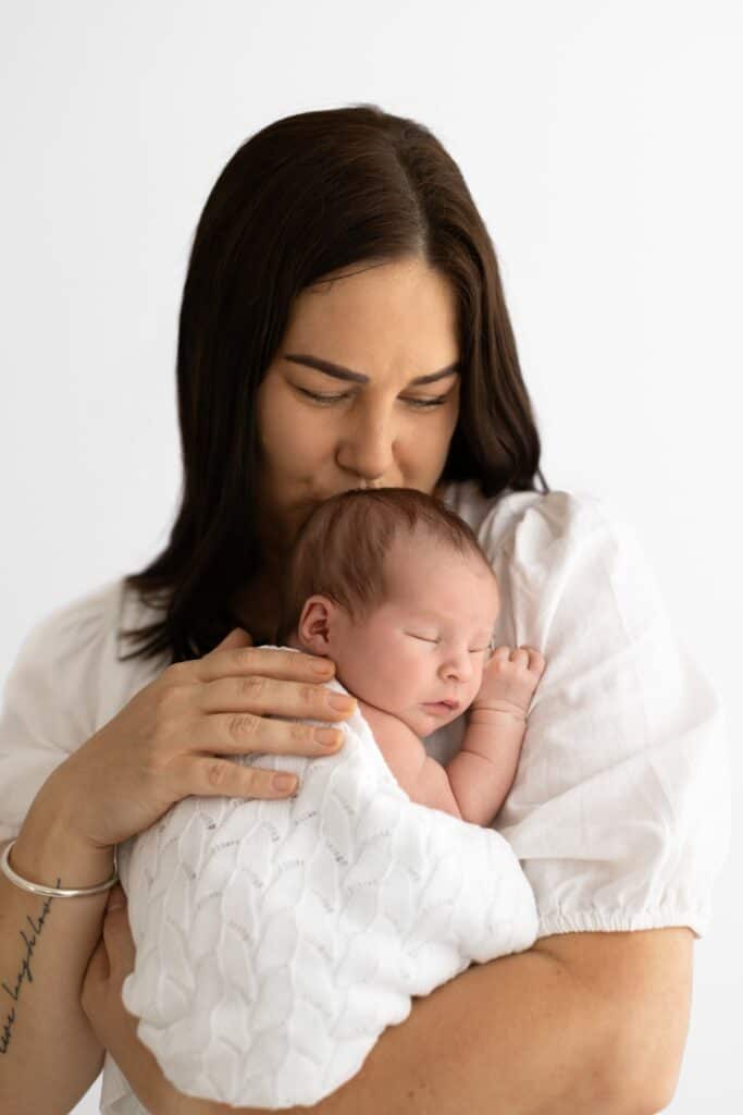 Mother cuddling new baby on white background in melbourne photography studio