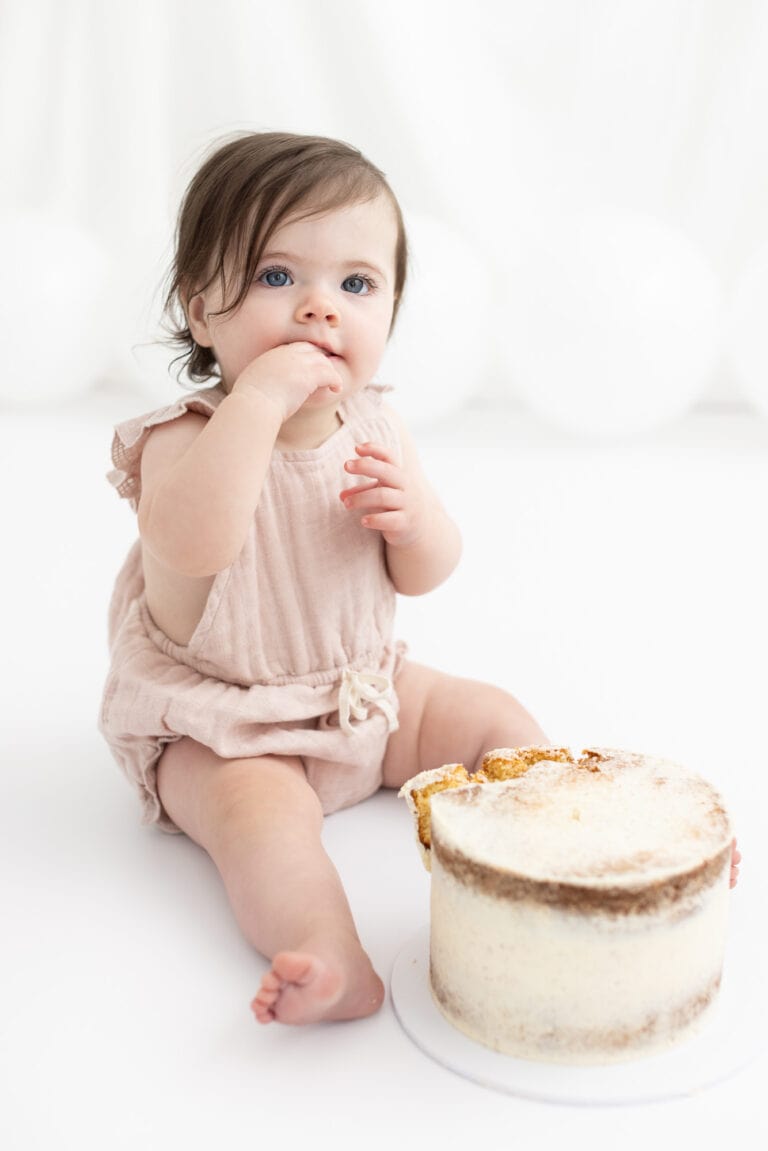 one year old sitting in front of cake, eating cake during 1st birthday cake smash photography session in Pakenham