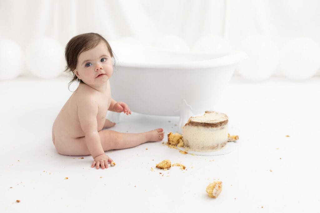 one year old sitting in front of white clawfoot bath, during 1st birthday cake smash photography session in Pakenham