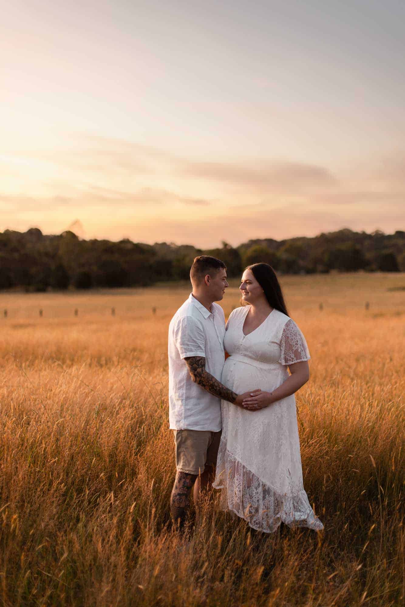 A couple embracing the woman's pregnant belly in field with long grass during a golden sunset
