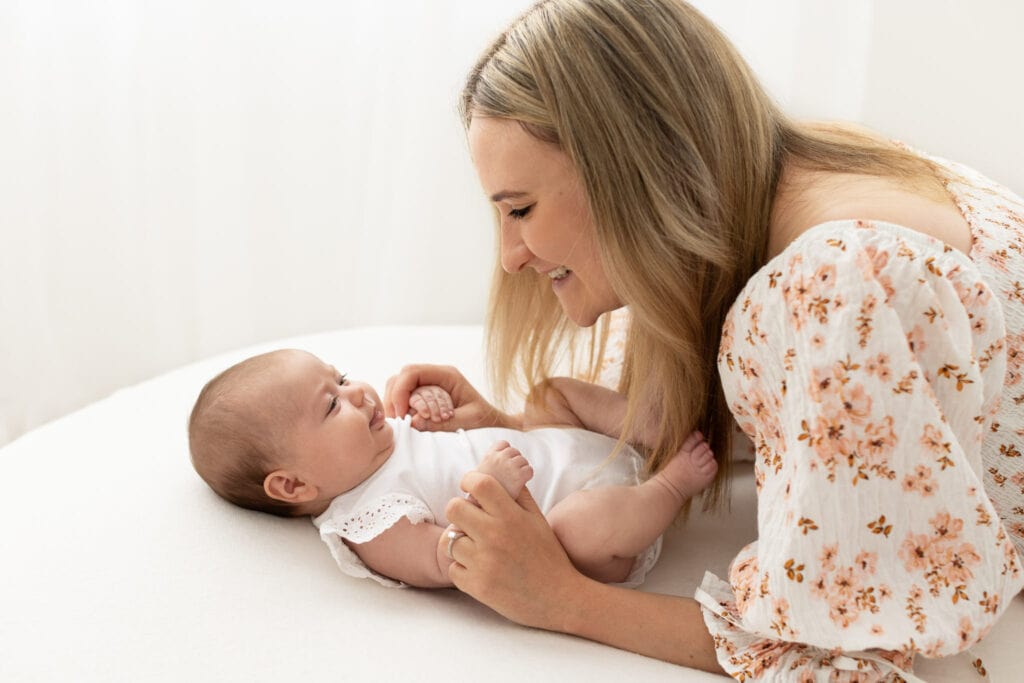 Mum looking down smiling at baby daughter on white blanket during melbourne motherhood photoshoot